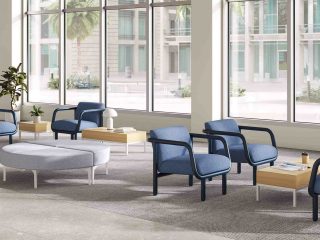 Waiting room with blue and yellow chairs and grey circle ottoman. Room has large windows.